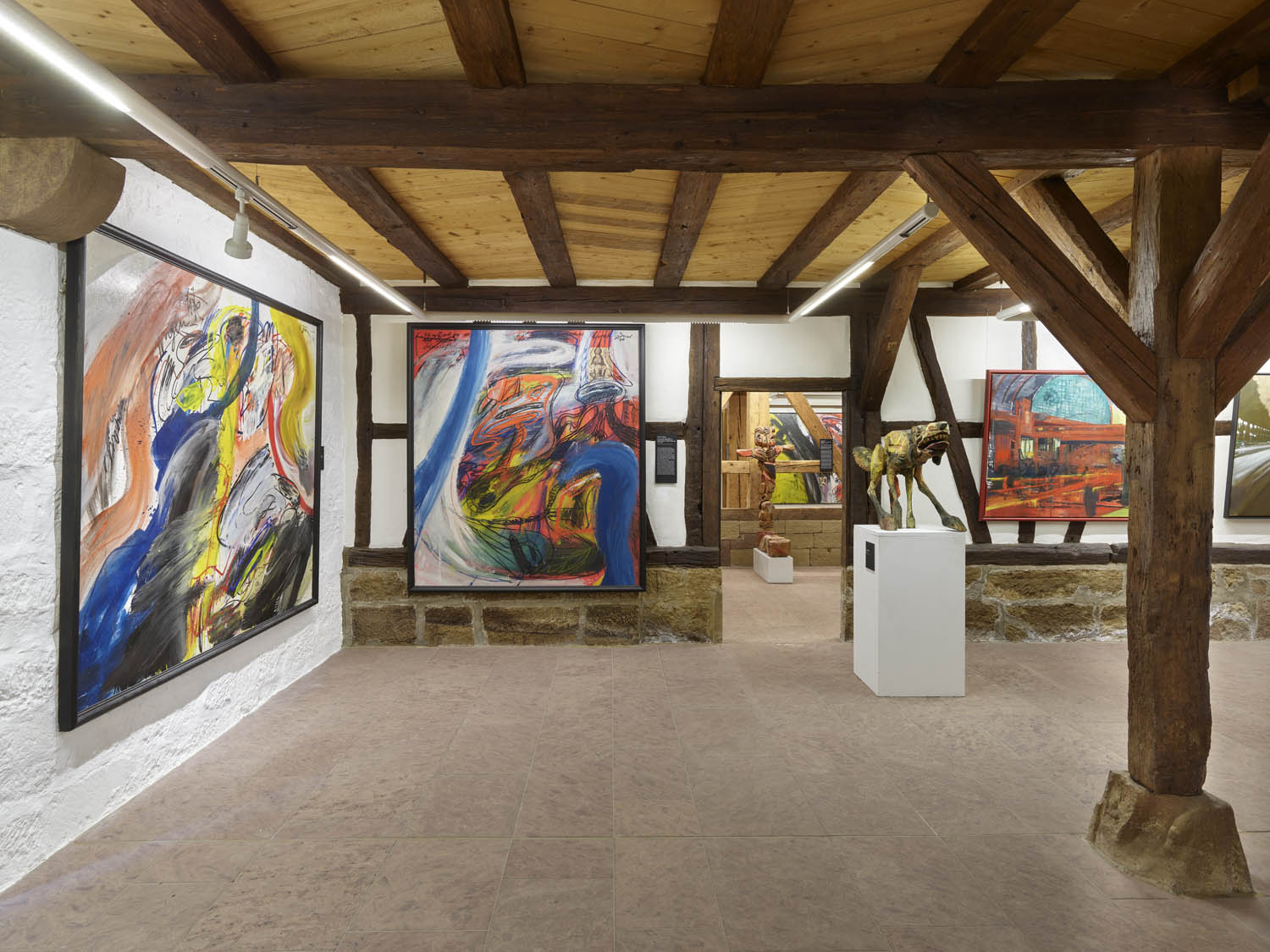 Perspektivischer Blick in ein Museum, mit großformatigen neoexpressionistischen Gemälden und Holzskulpturen